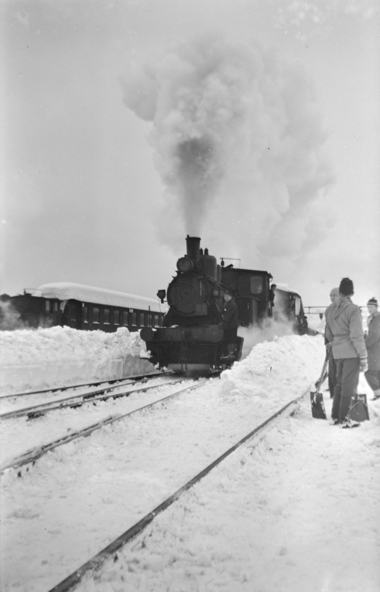 Snøryddingsmannskaper og snøryddingstog trukket av damplokomotiv type 25a på Trondheim stasjon.