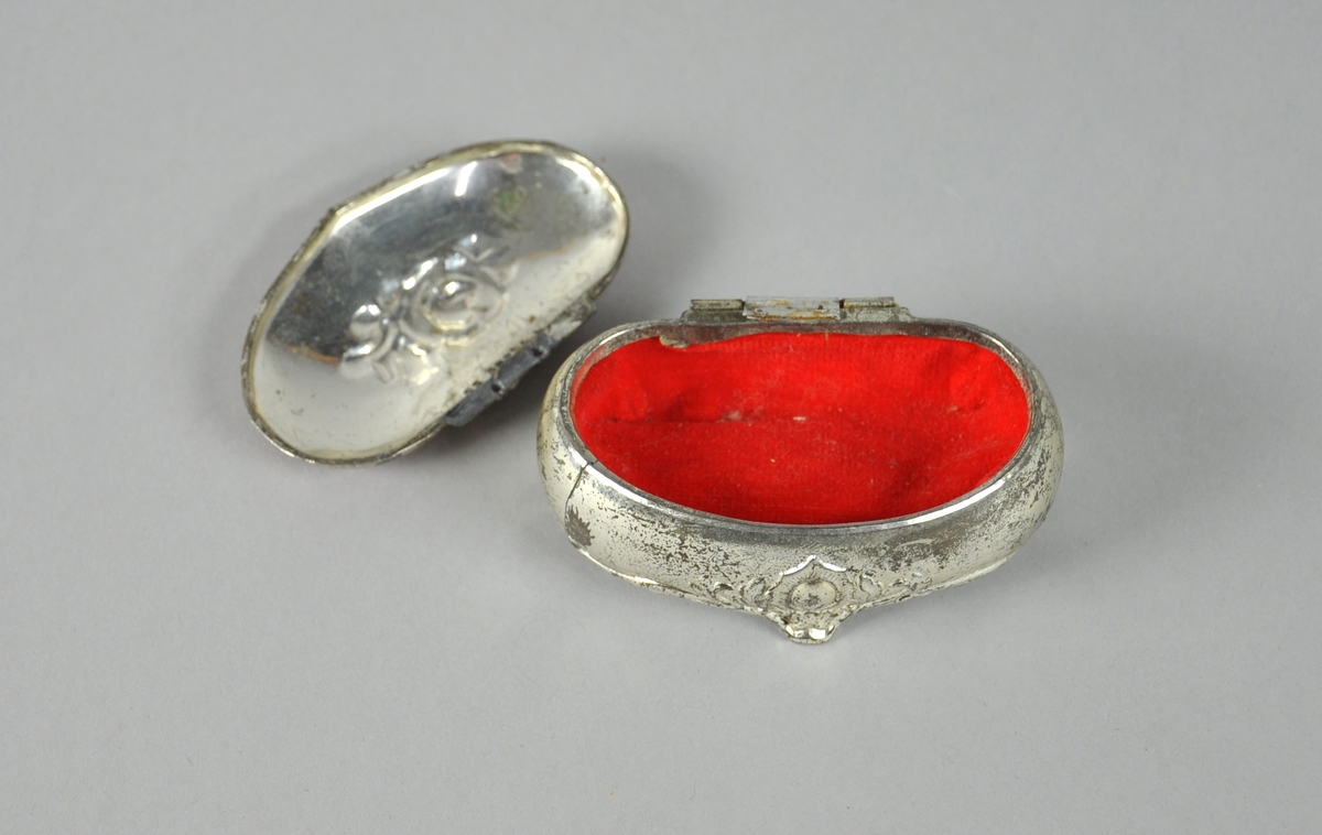 Ovalt, hjerteformet smykkeskrin med rødt lokk med innstøpt sølvrose. Skrinet har tre ben og utskåret blomsterdekor, og er foret med rød fløyel. Lokket har hengsel som er brukket og forsøkt reparert.