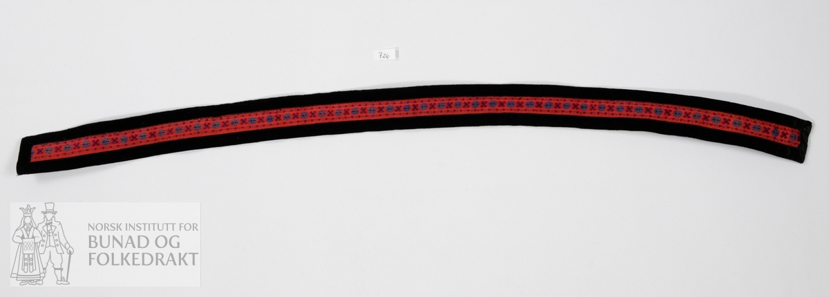 Belte. Vevd bånd med rød bunn og mønster i fargene fiolett, blått og svart. Kantet med svarte fløyelsbånd. Foret på baksiden med svart bomull. Beltet har sekundære endringer, blant annet er det stivet med vlieselin (limstoff). Beltet lukkes med to hekter, begge er intakte. Maskinsøm.