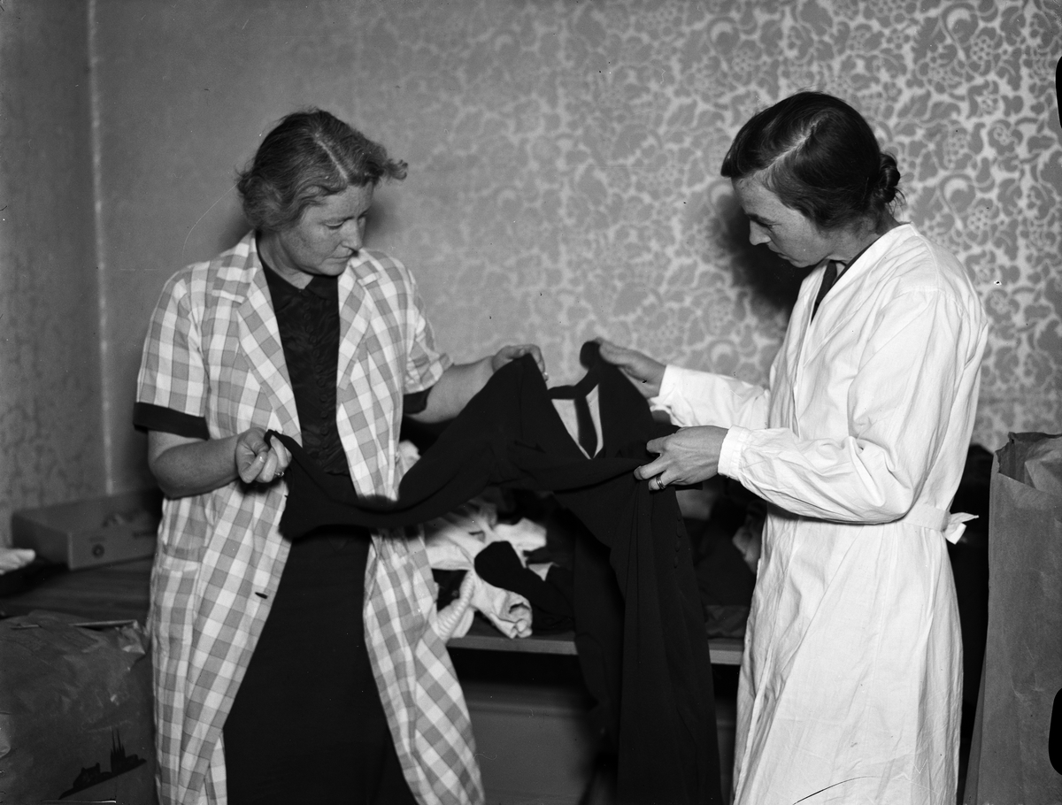Johanne Grieg-Cederblad och Bothild Fredriksson granskar ett klädesplagg som samlats in av Svenska Norgehjälpen, Kungsgatan 12