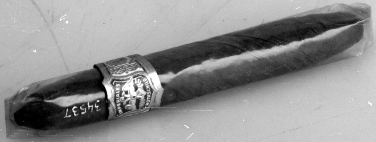 Sigaren er innpakket i cellofan med forseglede ender. Rundt sigaren gull-, rød- og hvitfarget mavebelte på utsiden av cellofanpakningen.