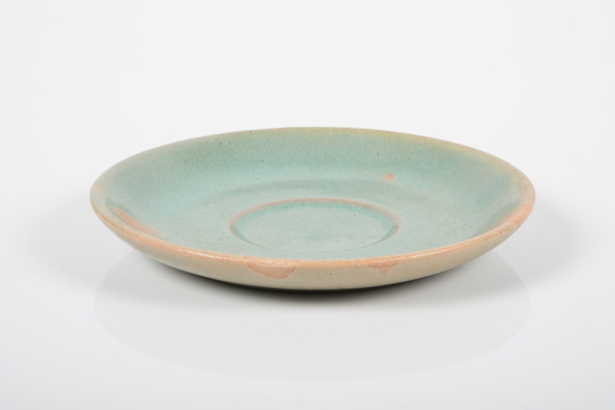 Rund skål i keramikk med grønn lasur. Skålen har spor etter tre knotter på bunnen, usikker funksjon. En hakk på oversiden (produksjonsfeil).