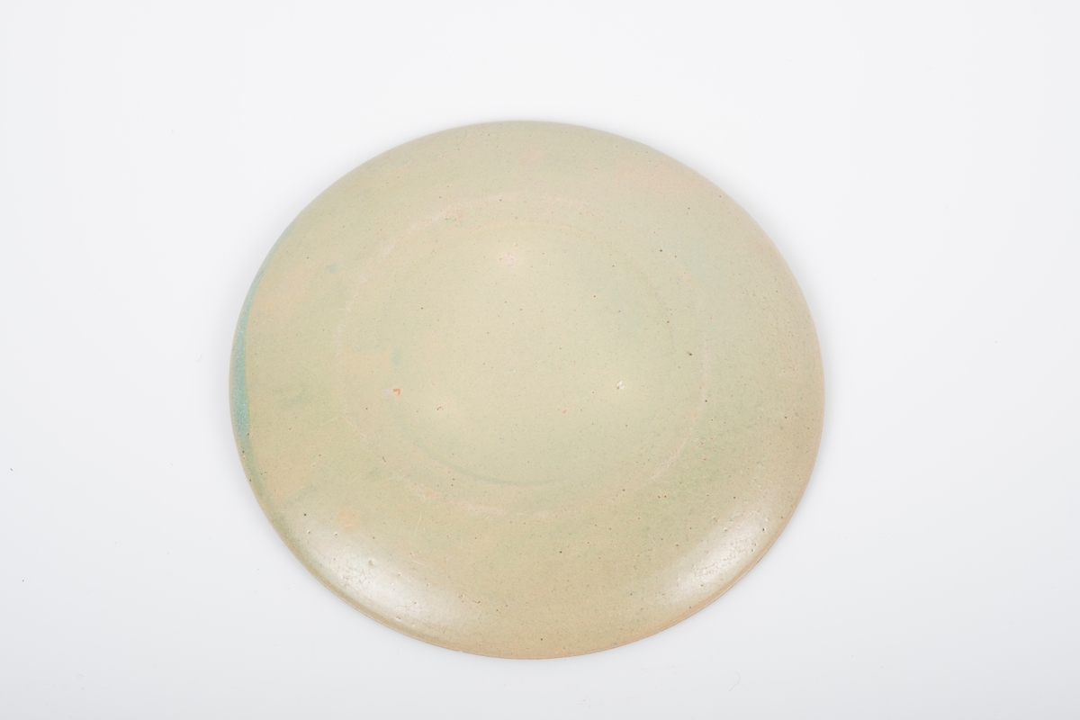 Sskål i keramikk med grønn lasur. Spor etter tre knotter på bunnen, usikker funksjon. Bunnen har matt overflate.