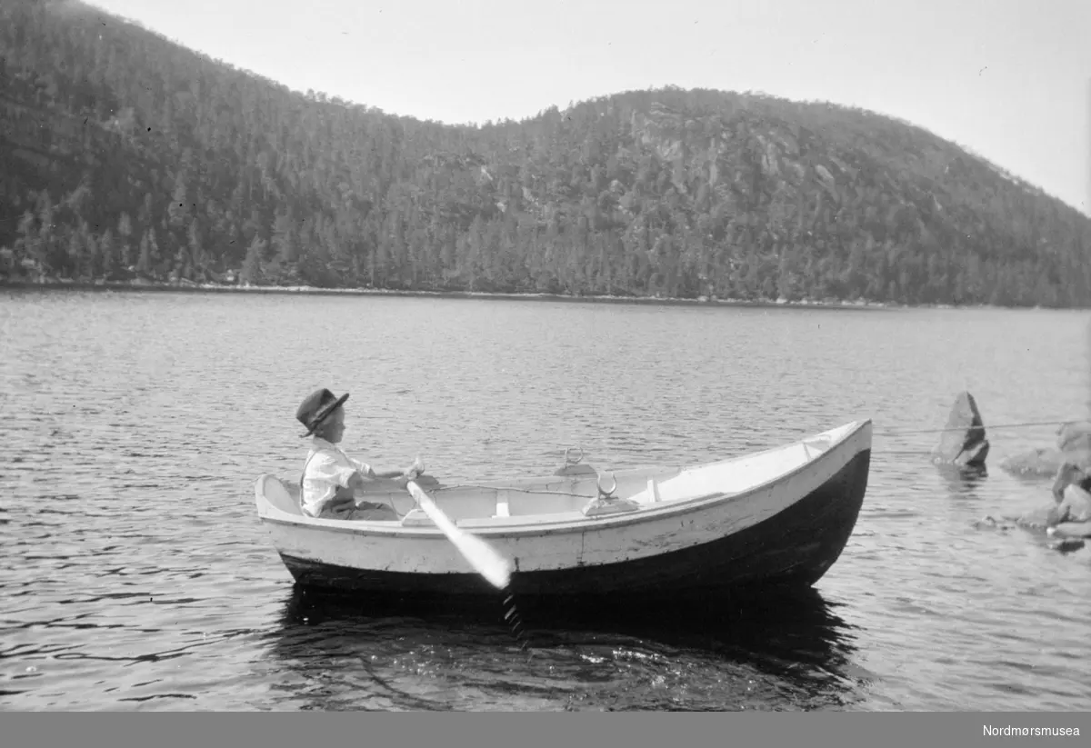 Foto av en ung gutt med hatt sittende bak årene i en liten robåt. Fra Sverdrupsamlingen ved Nordmøre museums fotosamlinger.