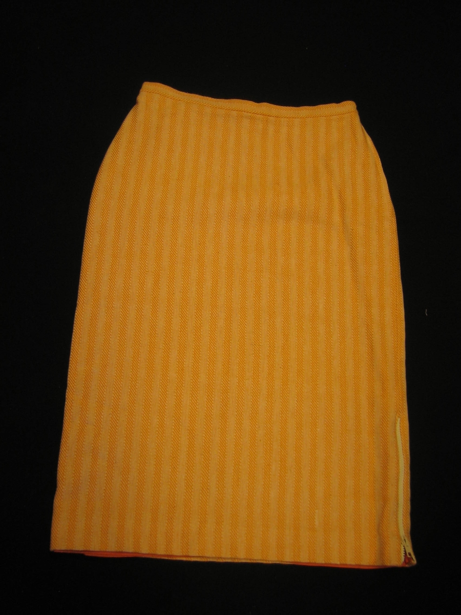 Orangegul sidenfodrad rak kjol i bomull. Tyget är vävt i kypert och tuskaft i 10 mm breda ränder. Kjolen har två sprängveck bak och dragkedja i vänster sida och en 25 mm bred linning med knapp och knapphål. Kjolen är försedd med ett sprund med dragkedja i vänster sida.