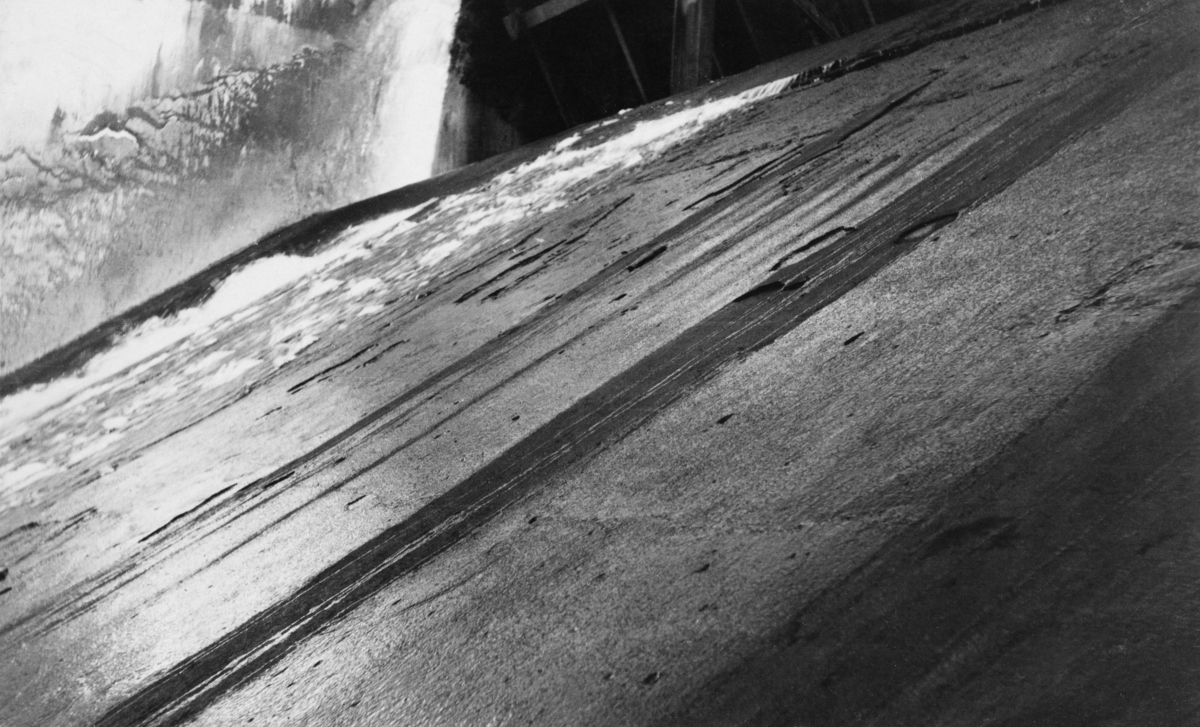 Detalj fra tømmerløpet i kraftverksdammen som ble bygd ved Osfallet i elva Søndre Osa i Åmot kommune i Hedmark.  Fotografiet er tatt i september 1915, et snaut år etter at kraftverket ble satt i drift.  På opptakstidspunktet var det åpenbart liten vanngjennomstrømming i elva, slik at en lett kunne se den glatte betongen som bare delvis var dekt av et tynt vannslør.

Osfallsdammen ble ødelagt under vårflommen i 1916, og dambruddet forårsaket store skader på det nye anlegget, noe som innebar betydelige økonomiske tap for utbyggerne, Åmot kommune.  Mer informasjon om kraftutbygginga ved Osfallet og det påfølgende dambruddet finnes under fanen "Opplysninger".