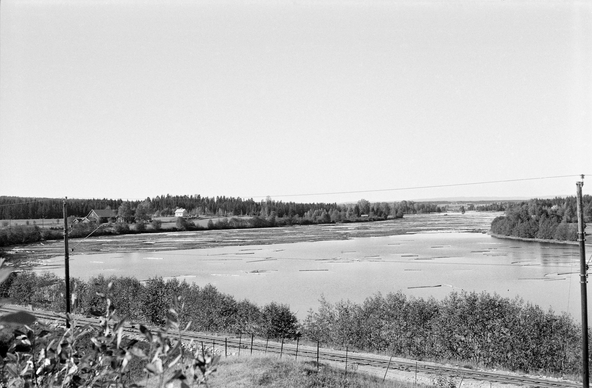 Opphoping av fløtingstømmer på Glommas vannspeil, like ovenfor Funnefossdammen i Nes kommune på Romerike.  Fotografiet ble tatt i 1959.  I forgrunnen ser vi jernbanetraseen, som her går på den sørøstre sida av elveløpet.  Til venstre i bildet ser vi et gardstun, antakelig på en av Sandaker-gardene.