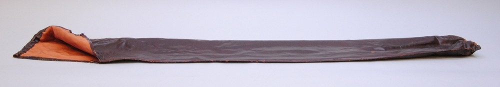 Fodral till fana. Fodralet är rektangulärt med en nedvikbar flik vid öppningen. Runt öppningen finns en kanal för att kunna trä i ett snöre och dra igen öppningen med. Snöre saknas. Utsidan är täckt av en brunsvart plastig yta. Insidan är laxrosa textil. Tillhör fana Jvm 21169:1.