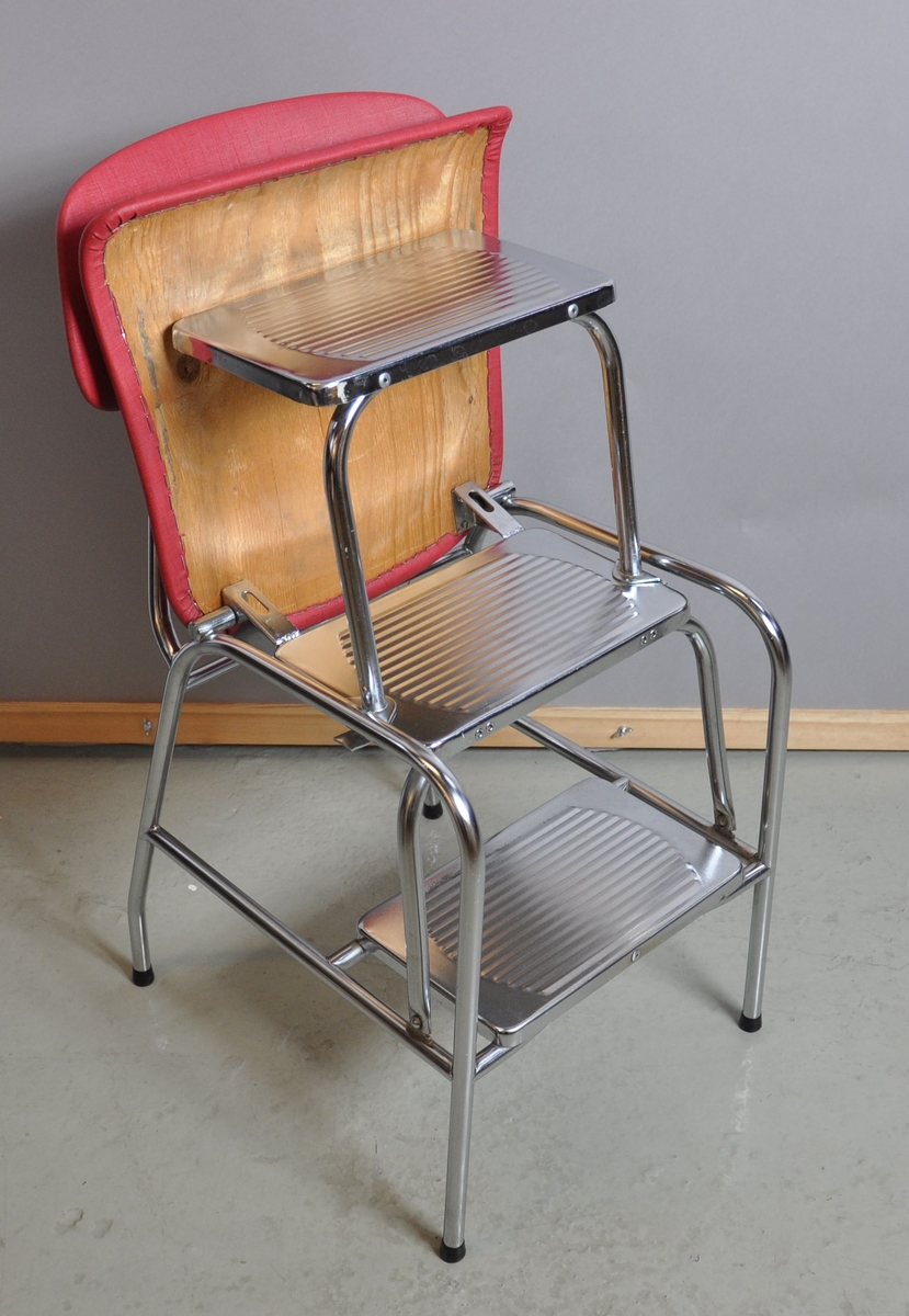 Husmorsstol. Stolen er laget av metall og trekt med rødt plastikksskinn. Setet kan løftes bakover slik at stolen fungerer som en trappestige med tre trinn.