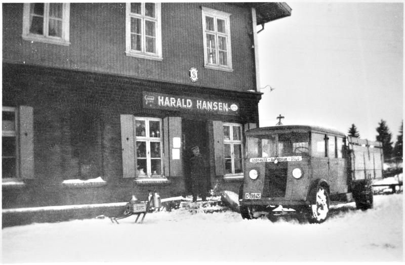 Svart-hvit foto av en bygning med en eldre bil stående foran.