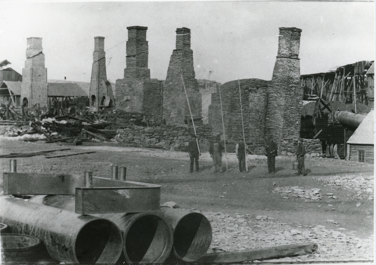 Ruinene av smeltehytta på Røros etter brannen i juni 1888. 5 arbeidere står vakt på malmplassen.