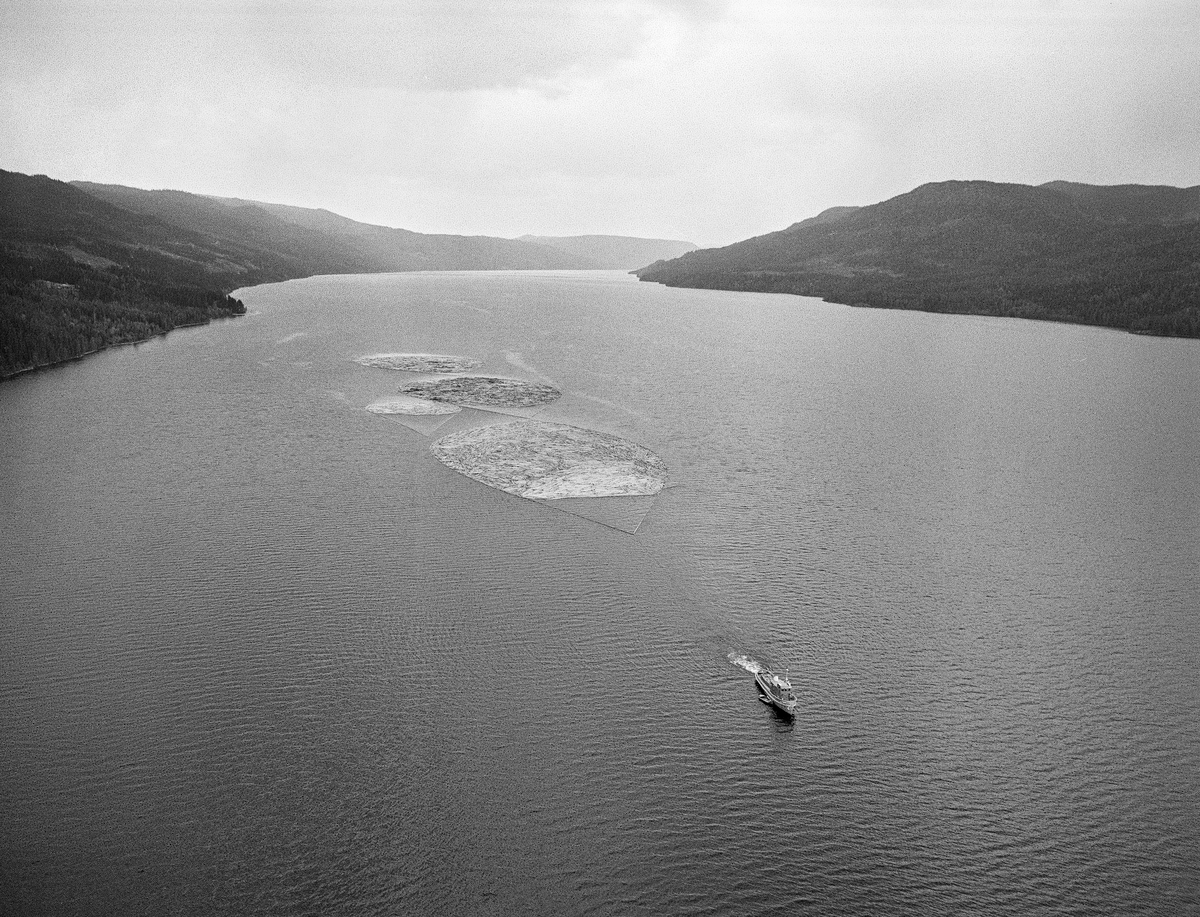 Flyfotografi av slepebåten «Storsjø» på innsjøen  i Rendalen som den hadde fått navn etter.  I ei trosse bak i god avstand bak «propellvannet» bak fartøyet hang slepet, som besto av en stor, to mellomstore ringbommer med fløtingstømmer.  Slepene var tunge.  I dampdriftsperioden, som for Storsjøs del varte fra 1912 til 1956, tok slepinga lang tid.  Dampmaskinen slukte nemlig 16 kubikkmeter ved i døgnet, og båten måtte gjerne ankres opp for bunkring av mer ved fra lagre langs strendene sørover.  I dieselepoken (fra 1957) brukte Storsjø brukte gjerne 30-40 timer på å buksere tømmer fra Åsheim i nordenden av sjøen til Åmot-grensa 36 kilometer lengre sør.  Gjennomsnittshastigheten var med andre ord cirka 1 kilometer i timen.  Tilbaketuren nordover sjøen, uten slep, var vanligvis unnagjort på to og en halv time. Slepetida var for øvrig avhengig av vær og vind, og av mannskepenes evne til å følge strømdraget i sjøen, den såkalte «råka».  I kraftig vind kunne bommene ryke, slik at løstømmeret ble spredt ut over sjøens vannspeil.  Under slike værforhold svarte det seg å legge båten og slepet mot land og vente på at vinden spaknet, eller rett og slett å la ringbommene flyte fritt.  Med den driftsaktiviteten som foregikk i rendalsskogene i 1950-åra kunne det går over tredve slike slep over Storsjøen i løpet av en sesong.  De siste åra, da det bare var massevirke til Borregaard som fortsatt ble fløtet, var antallet slep redusert til om lag en tredel av dette.  Fra gammelt av ble det sagt at det kunne gå 12-15 000 tylfter tømmer i hvert slep, men med stadig større massevirkeandel ble det mer småtømmer og dermed flere stokker i ringbommene.

Mer informasjon om slepebåten «Storsjø» finnes under fanen «Opplysninger».