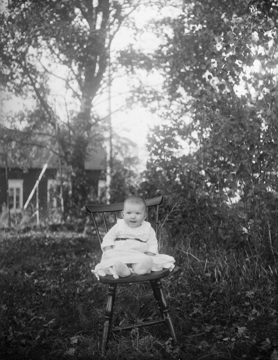 Slöjdar Jansons flicka sitter i stol i trädgården, Altuna by, Altuna socken, Uppland 1921