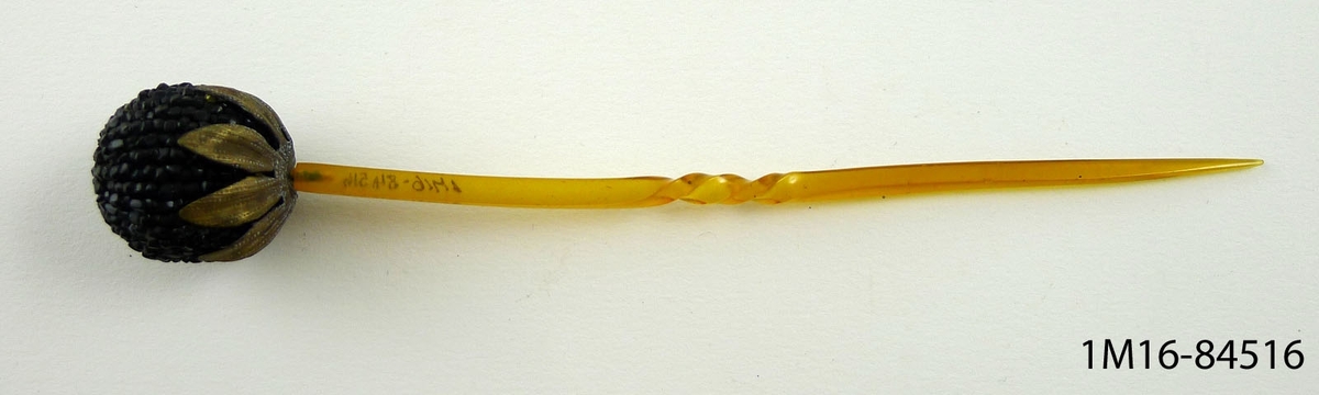 Hårprydnad med nål av celluloid och runt huvud täckt med små stenkolspärlor och blad av mässing.