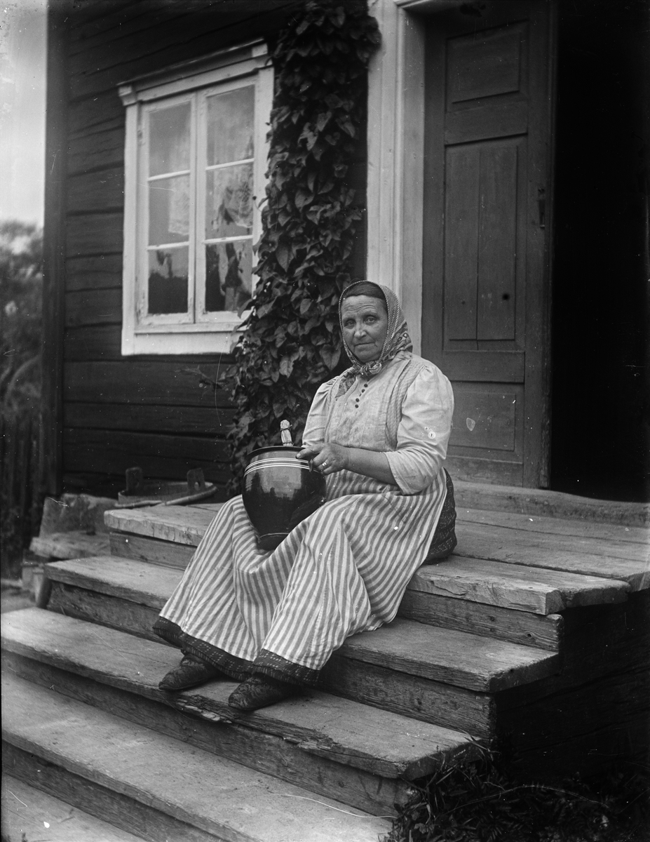 Äldre kvinna sitter på yttertappan med kruka, Uppland