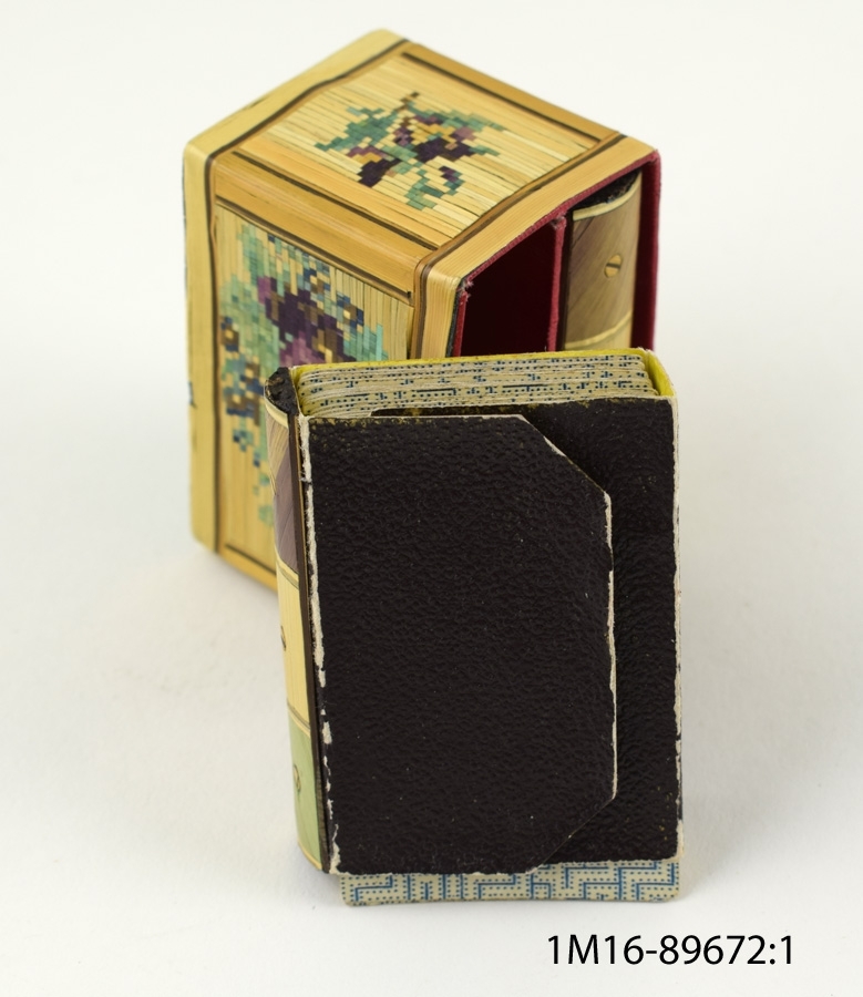 Två små kortlekar som förvaras i låda i formen av en liten bokhylla med ett fack för vardera kortlek. Blommotiv på lådans alla sidor.
