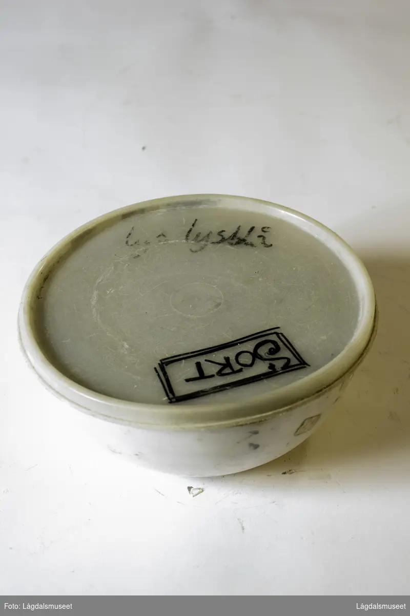 Plastbolle med lokk med uttørket pipeleire i fargen svart. Pipeleiren ble brukt til begitting av keramikken.