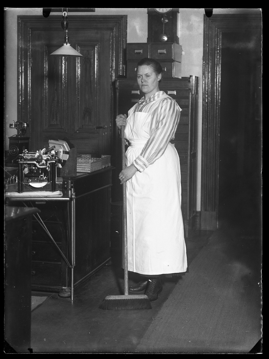 Fru Johansson porträtterad med sopkvast på ett av Alingsås Bomullsväveris kontor.