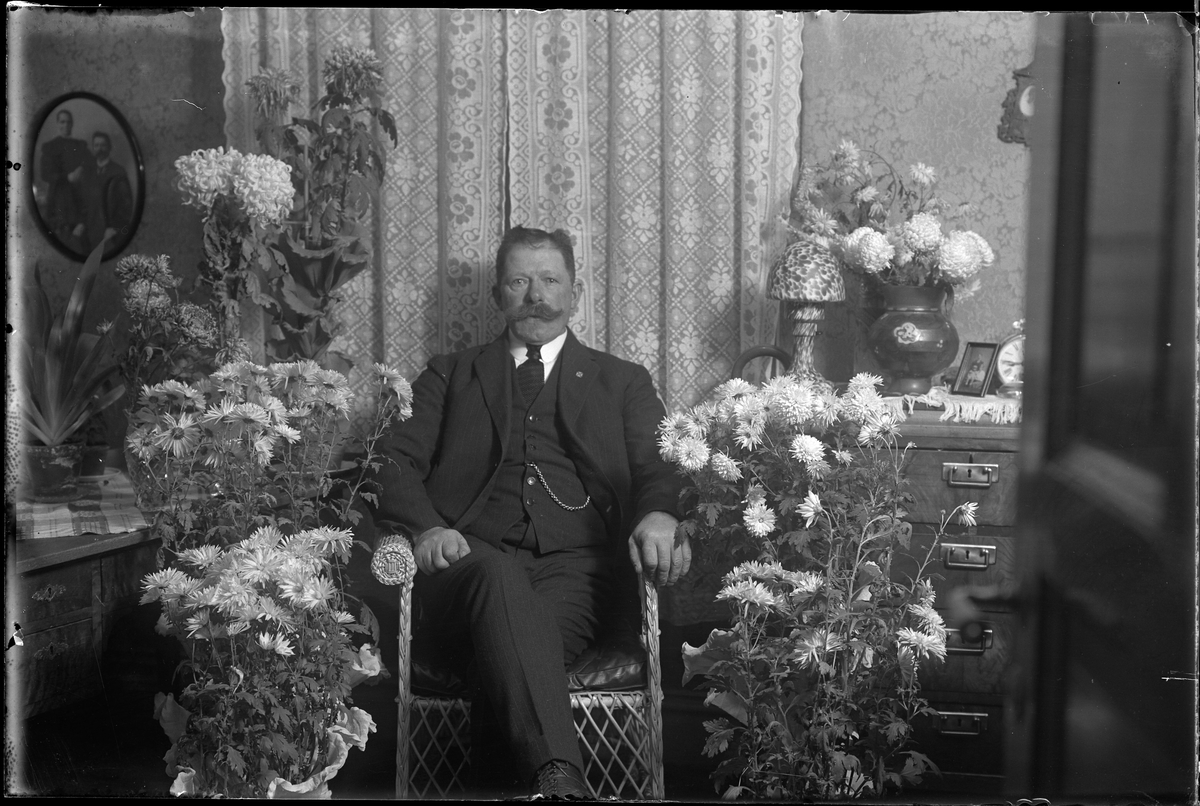 Karl Dahlgren sitter i en korgstol, omgiven av blommor och fotograferad i samband med sin 60årsdag.