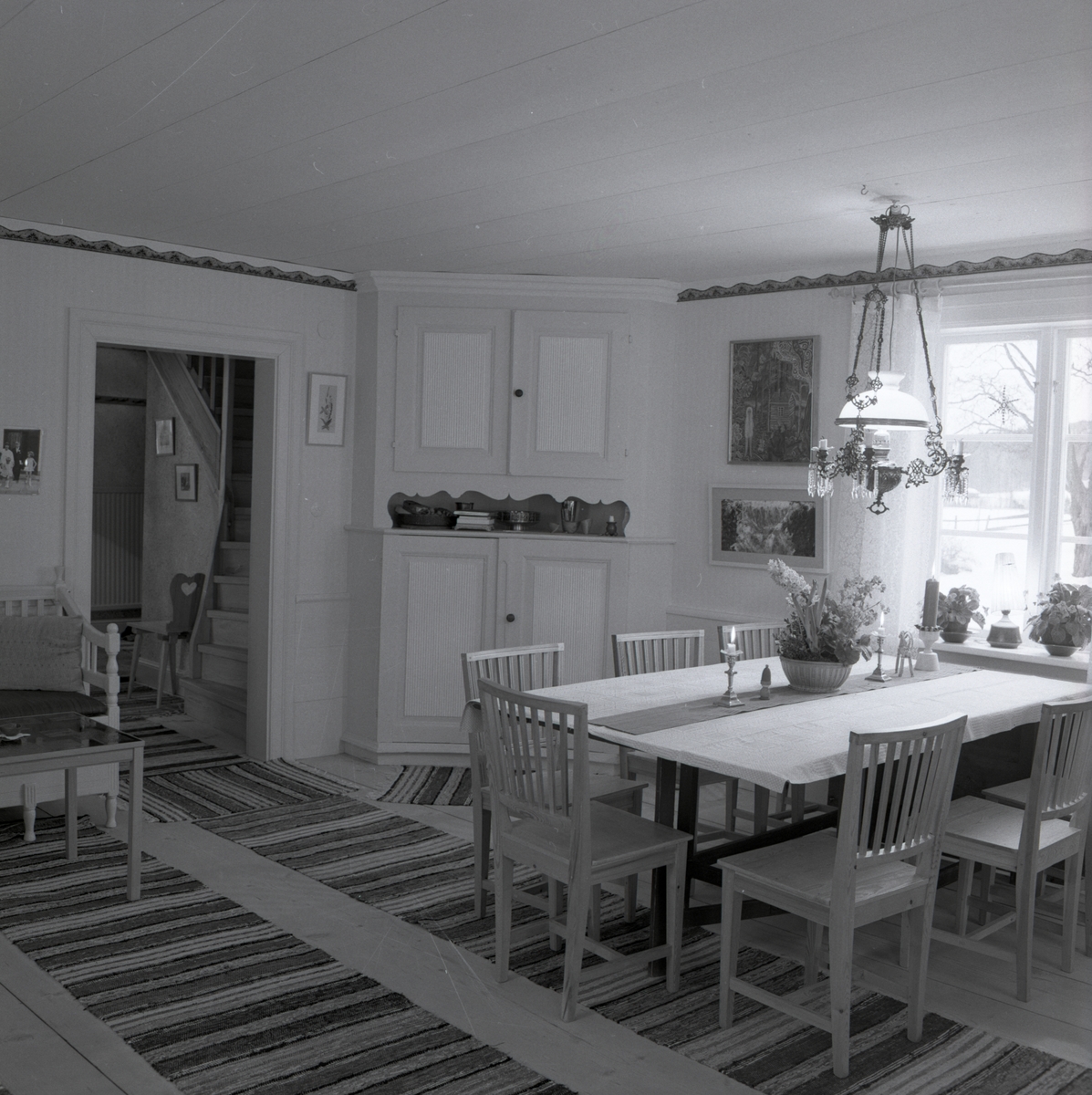 Ett rum på gården Sunnanåker med ett hörnskåp samt ett bord med stolar och taklampa, januari 1970.