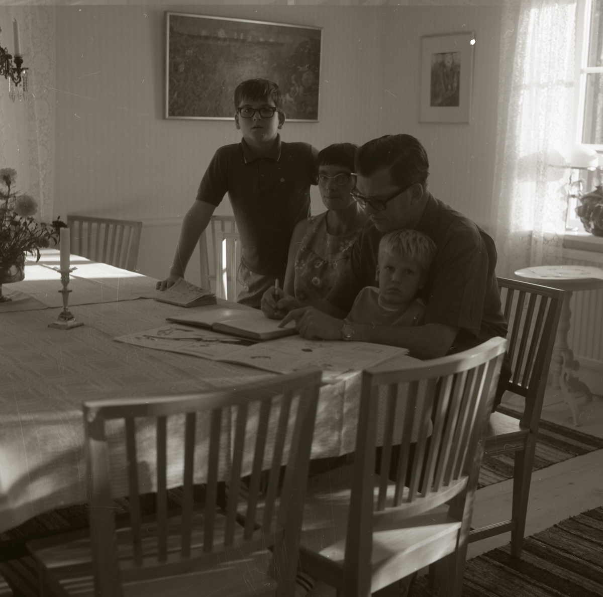 En familj har samlats vid ett bord och skriver i ett block, 1967-68 vid gården Sunnanåker.