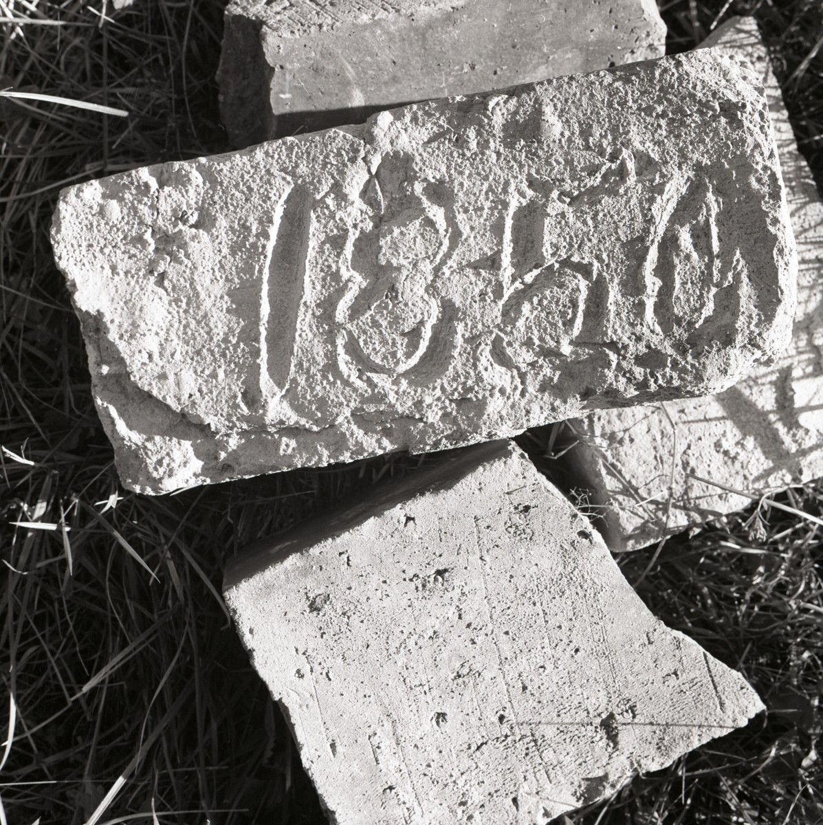 Några tegelstenar ligger i gräs och på den ena är inristat årtalet 1850, Rengsjö 1967.