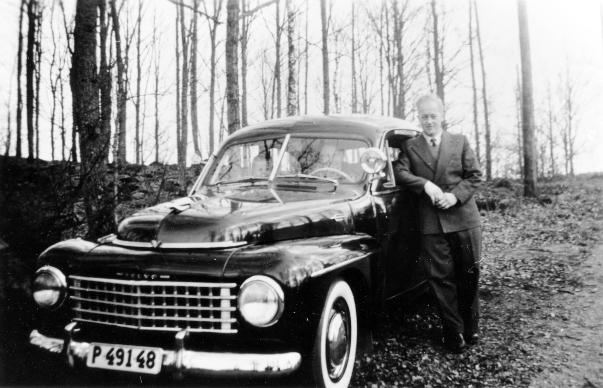 Nils Sahl, i kostym, står avslappnat bredvid sin andra bil, en PV med registreringsnummer P41948. I bilen syns en kvinna och ett litet barn.