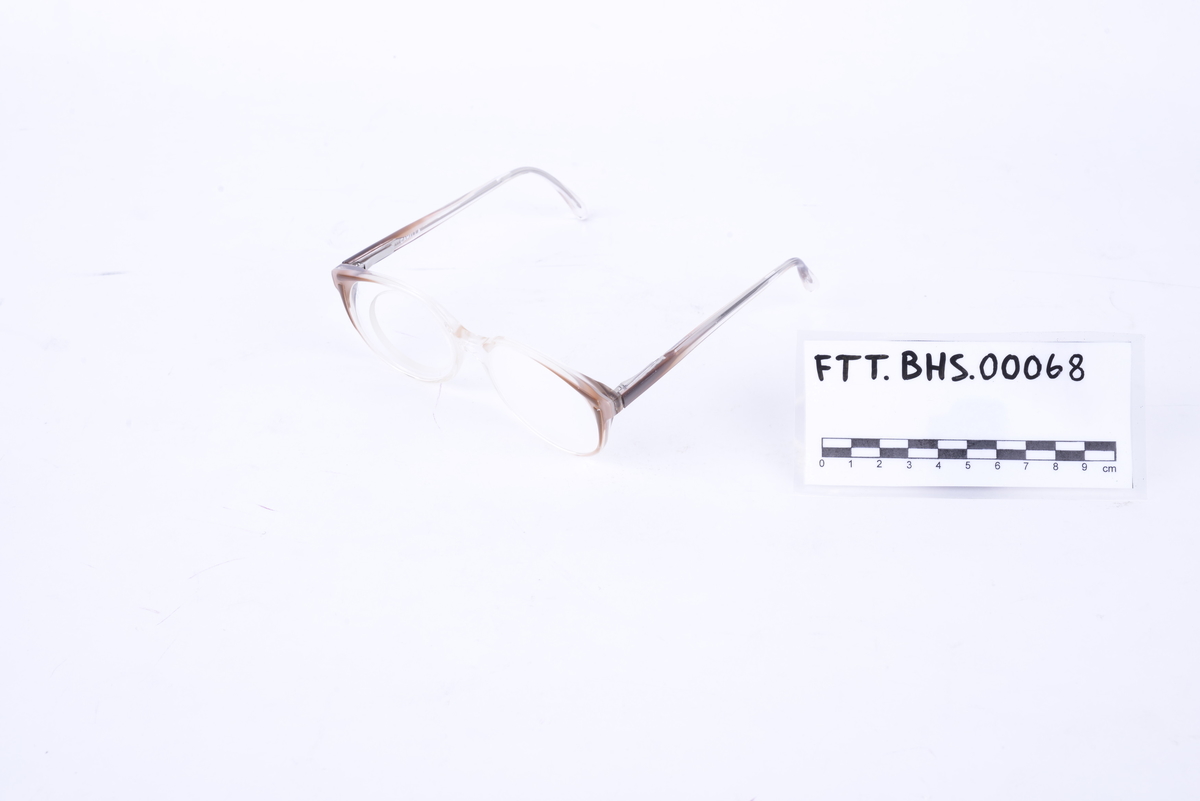Brille i hvit og brun plast med frostet glass på venstre side. Glass med hull for å sette inn ulike linser på høyre side.