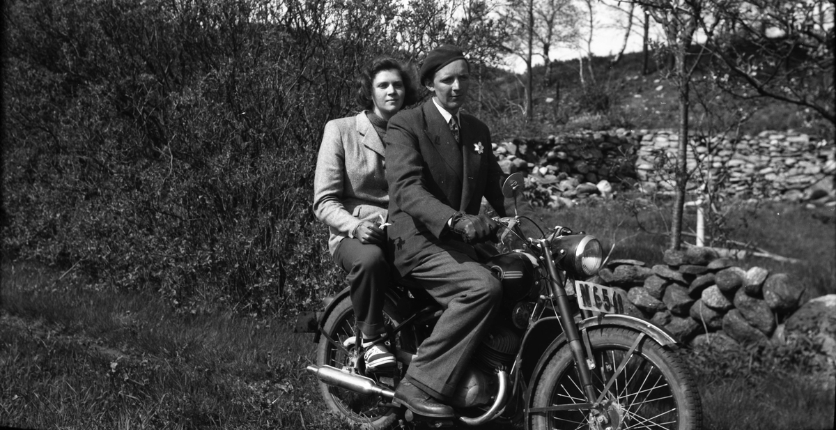 Syskonen Ivar och Margit sitter på en motorcykel om våren vid en husruin. De har varsin pingstlilja; Ivar har fäst sin på kavajslaget och Margit håller sin i handen.