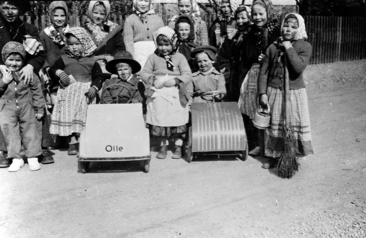 Ett femtontal barn utklädda till påskgummor och påskgubbar varav två pojkar i sina lådbilar.