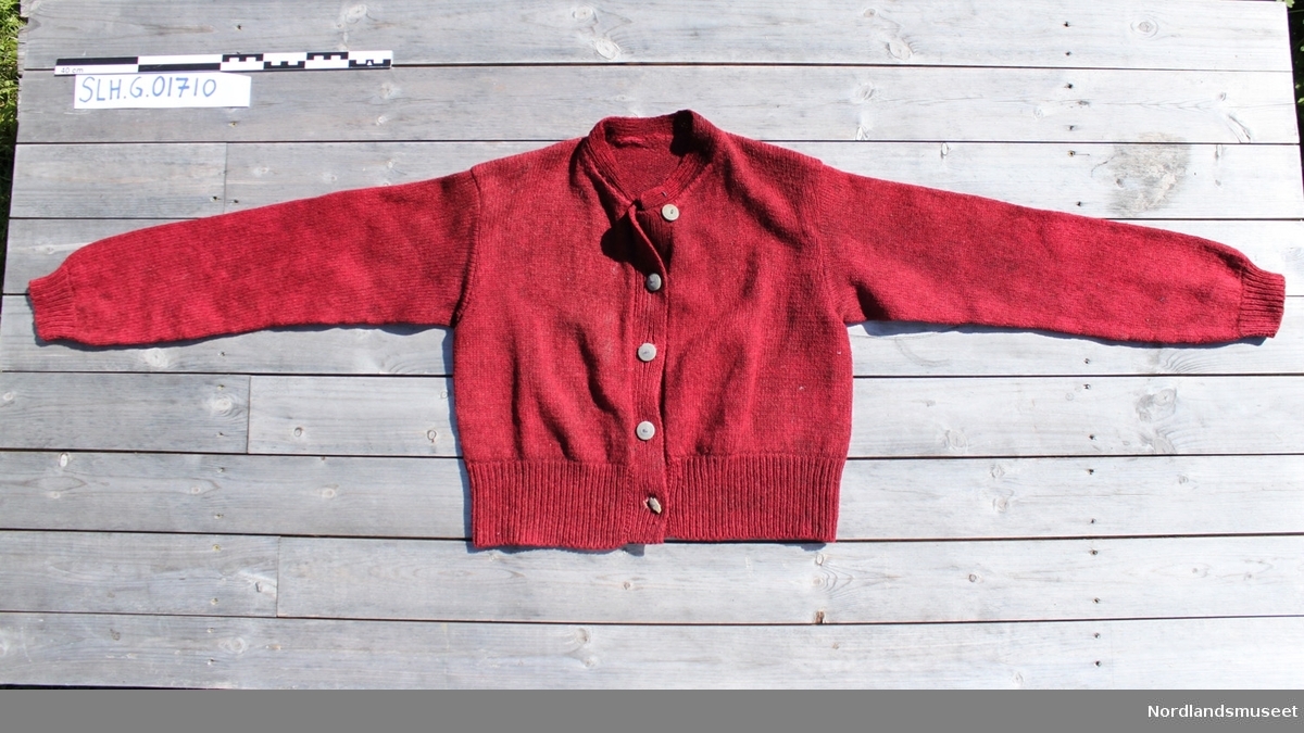Rød strikket jakke med knepping foran. Mandarinkrage. Knapper i tre. Èn knapp er ødelagt.