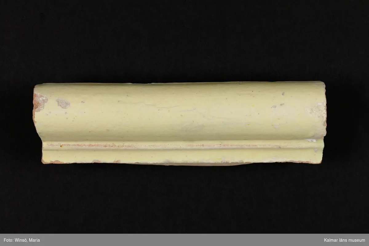 KLM 38928. Kakel. Till kakelugn. Svagt gulgrön blyglasyr på röd lergodsskärv. Drejad rump.

Förteckning över samtliga kakel, med mått inom parentes, gjord i samband med inventering 1997:  
:1.  3 st. fasadkakel         (26x21x5 cm)
     2 st.  -"-                    (26,5x21,5x6 cm)
     1 st.  -"-                    (26,5x21x5,5 cm)
     1 st.  -"-                    (26,5x20x6 cm)
     2 st.  -"-  1/2 lod       (26,5x16,5x5 cm)
     3 st.  -"-  1/2 lod       (26,5x10x5,5 cm)
:2. 12 st. hörnfasad        (23x13x6 cm)
:3. 4 st. krönsims           (13x21,5x5 cm)
     1 st.  -"-                   (13x10,5x4 cm)
     1 st.  -"-                   (20x25x5 cm)
     1 st.  -"-                   (20x17x5 cm)
     1 st.  -"-                   (13,5x11x4 cm)
:4. 1 st. hörnkrönsims    (13x25x5 cm)
     1 st.  -"-                   (13x17,5x5 cm)
:5. 7 st. simser               (6x21,5x4,5 cm)
     1 st.  -"-                   (6x18x4 cm)
:6. 2 st. hörnsimser        (6x15x3 cm)
:7. 5 st. fotsimser           (14,5x21,5x5 cm)
     1 st.  -"-                   (14,5x15,5x5 cm)
:8. 4 st. hörnfotsimser    (14,5x20x5,5 cm)
:9. 45 st. fragment