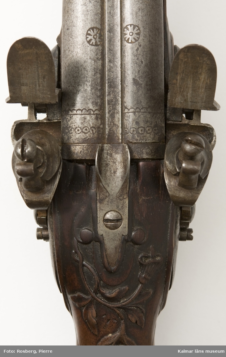 KLM 14477 Pistol. Dubbelpipig. Flintlås. Stocken med reliefdekor. Dekor på pipor och beslag. Datering: 1700-talets mitt.