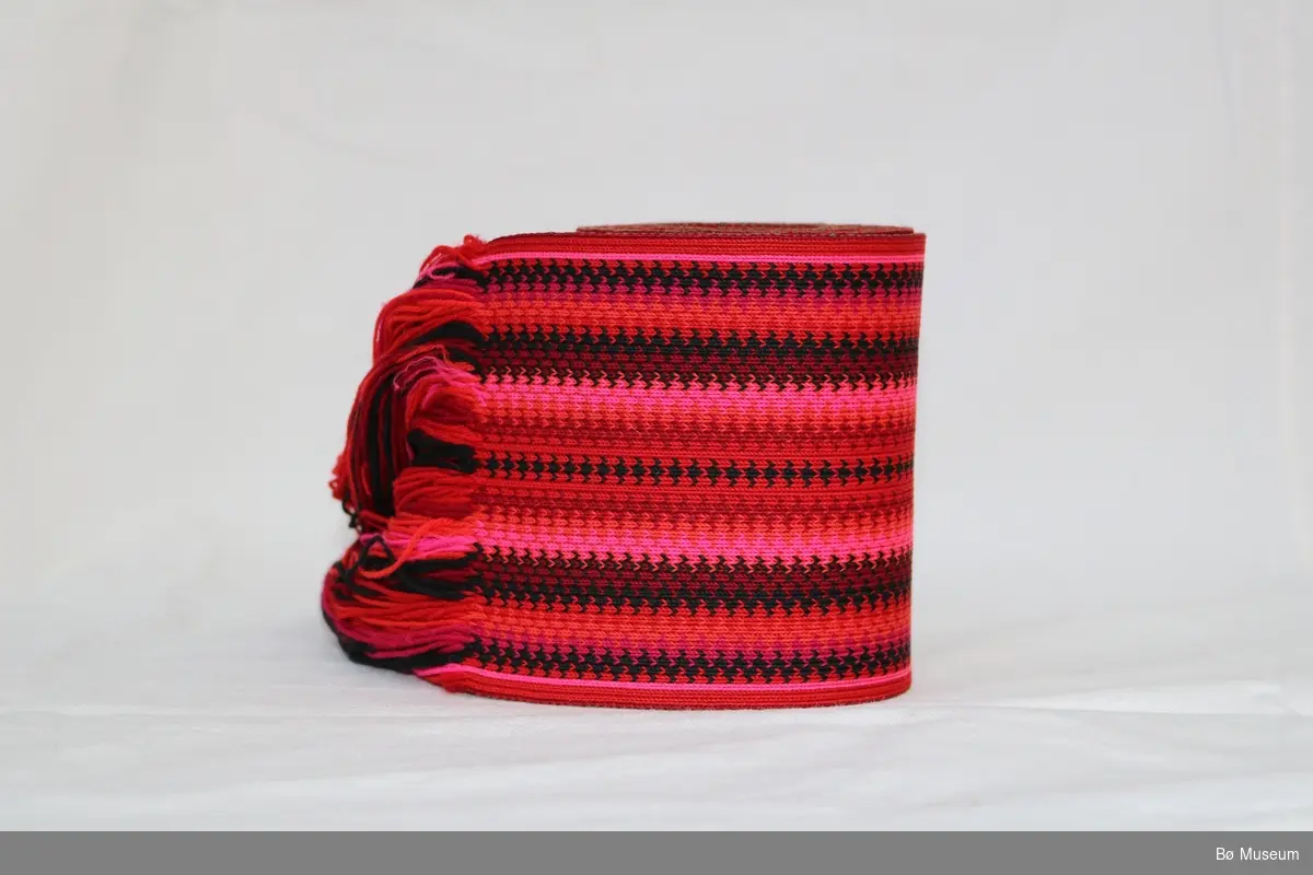 Stakkebelte med tafs i eine enden og mønster som består av striper og sikksakk-mønster. Type: Hælge Beltevevarbelte.