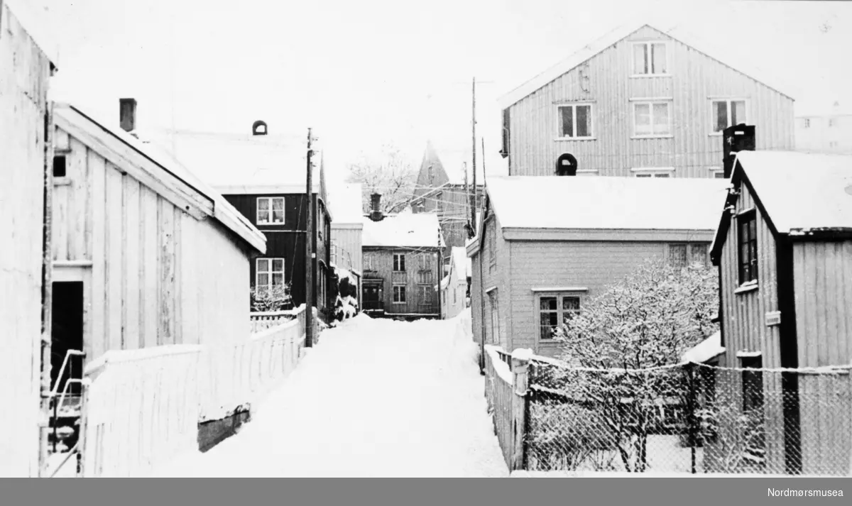 Foto fra en snødekt gateparti, antakeligvis fra Innlandet i Kristiansund. Fotoarkivet stammer fra Nordmørsposten, og inngår nå i Nordmøre museums fotosamlinger.