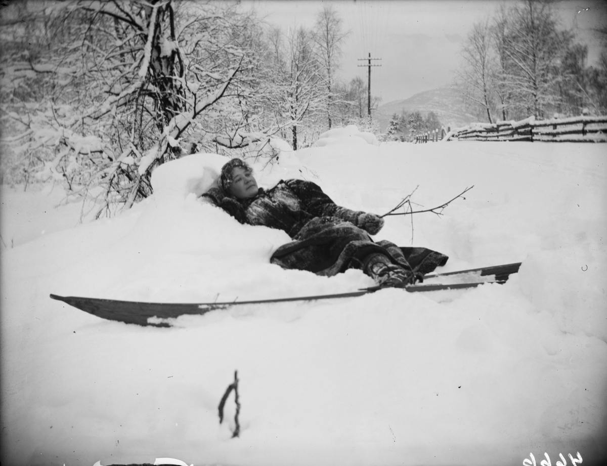 Kvinne ligger i snøen med ski på beina