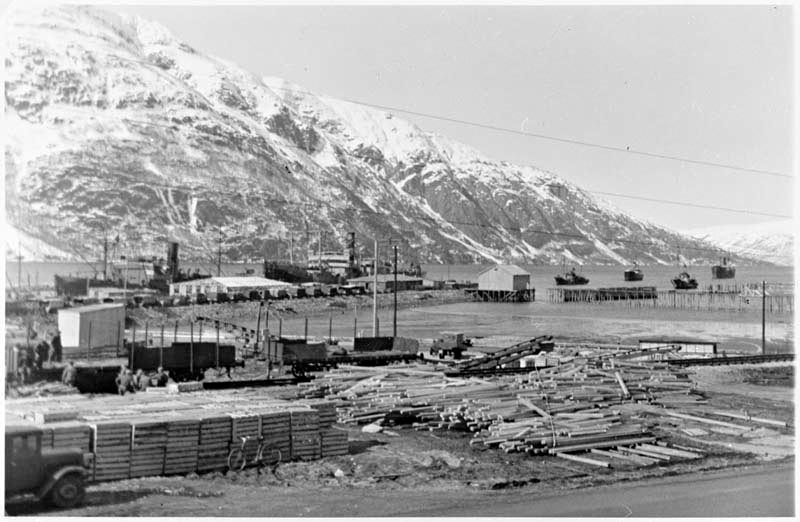 Bildet er tatt på kaia i Mosjøen under krigen, mange båter på fjorden. Mye tømmer lagret.