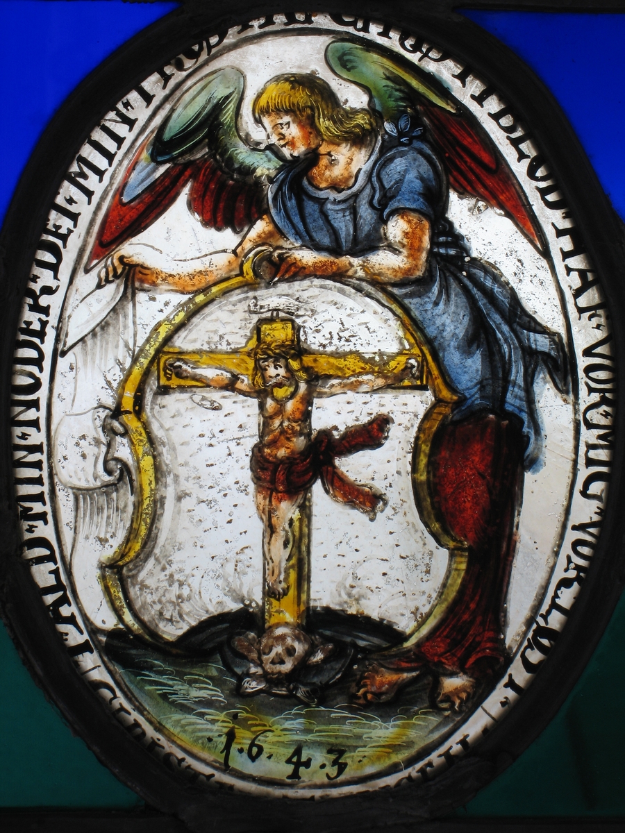 Kristus på korset i et prikket skjold, holdes av engel i blått og brunt, litt grønt på vingene.  Tekst rundt  feltet
