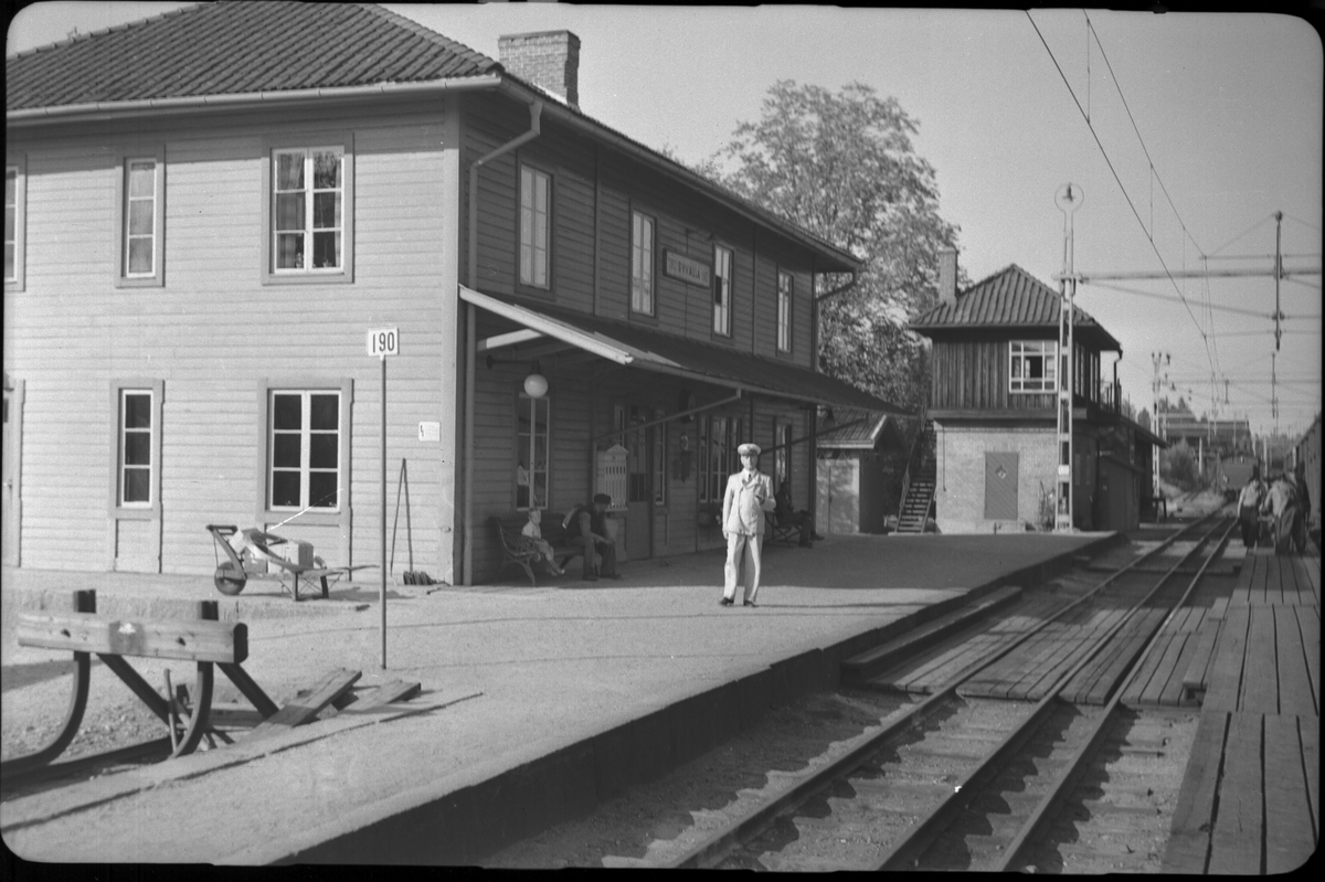 Byvalla station. Stationsinspektor i sommaruniform. Bortom stationen syns ställverkshuset.Treskensspår.