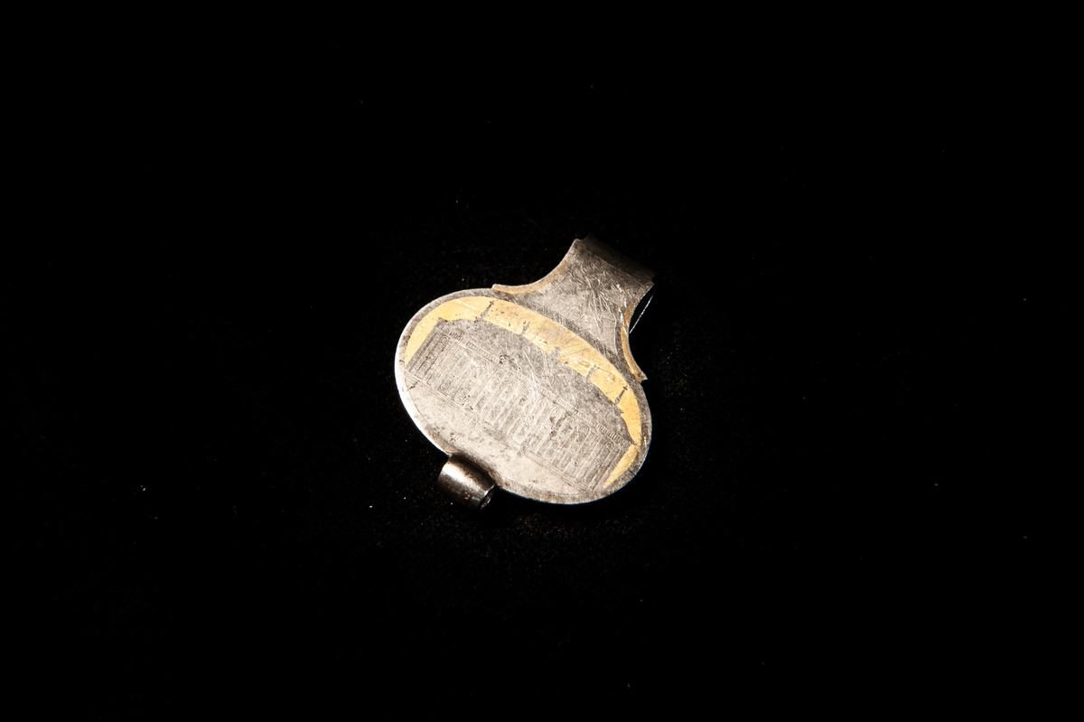 Oval hake, skärpkrok, prydd med tvåfärgad etsad bild av Riddarhuset, Stockholm.  Ovanför detta ett emblem med fackla och pil. Saknar helt märken eller stämplar. Haken har troligen använts för att fästa en dams klockkedja.