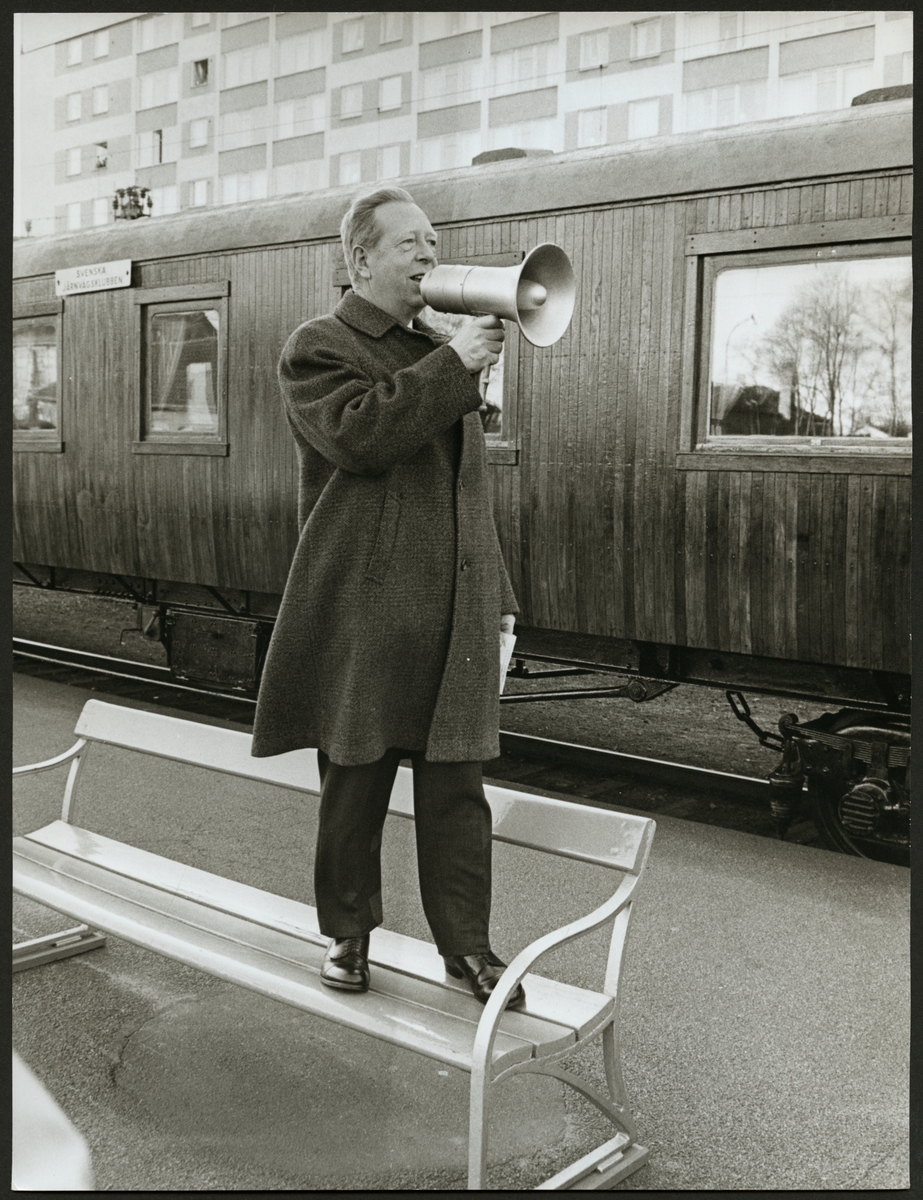 Framför personvagnen står en man med megafon på Centralstationen i Eskilstuna. Skylten på vagnen säger "Svenska Järnvägsklubben".