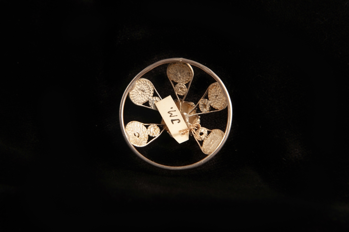 En malja av silver. Filigranarbete i form av fem "tungor" upp mot blomma i filigran. Stämplad på rundelns kant. JM.19973:a-e hör ihop.