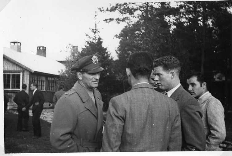 Kostymklädda män i samtal, en i uniform. Möjligen vid friluftsgården (friluftshotellet) i Mullsjö.
