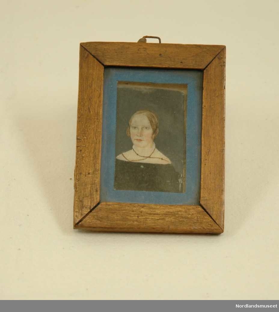 Miniatyr, malt portrett av ung kvinne. Blå paspartout, ramme i tre og glass. Tøyhempe til oppgeng.