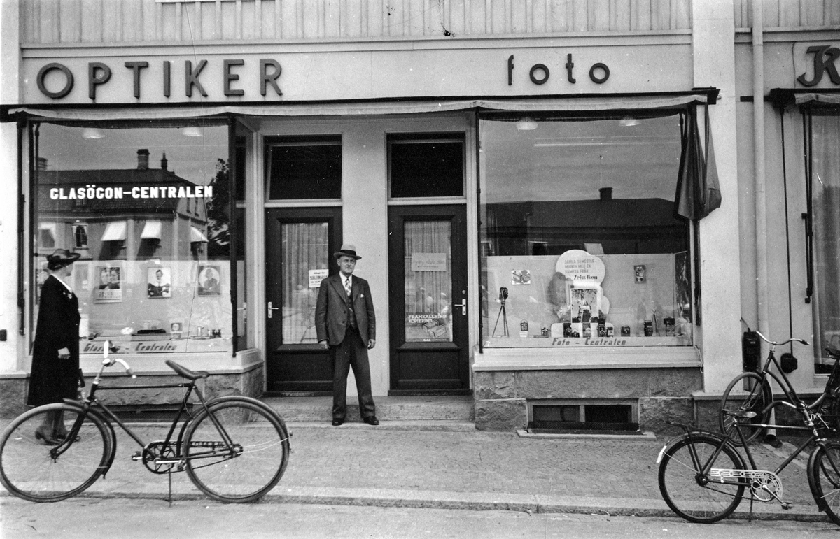 Exteriörbild på Foto-Centralen i kvarteret Kronan 14. En kvinna tittar på varorna i skylten och en man står vid entrén.
