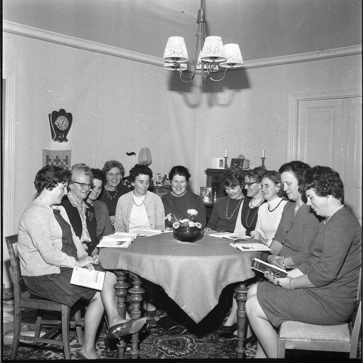 Elva kvinnor sitter runt ett bord. Det är Centerns Kvinnoförbund i Vireda som håller kurs i blomsterodling hemma hos fru Elsie Wier-Johansson. Cirkelledare är studiesekreterare Birgit Karlsson i Björkenäs som sitter till vänster. Till höger sitter Anita Nilsson.