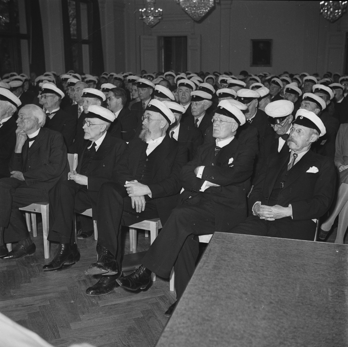 Flera personer iförda studentmössor sitter i samlingssal, Östgöta nations 300-årsjubileum, Uppsala 1946