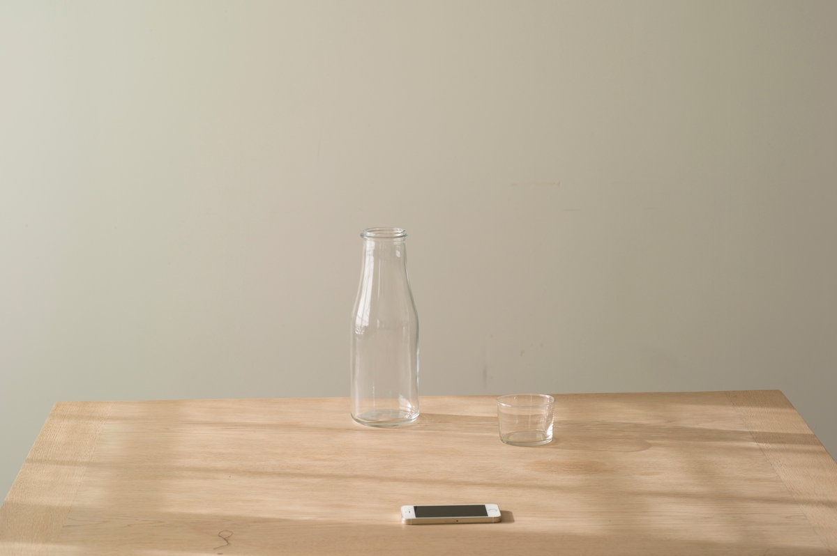 Motivet viser et bord med en vannkaraffel, et glass og en mobiltelefon.