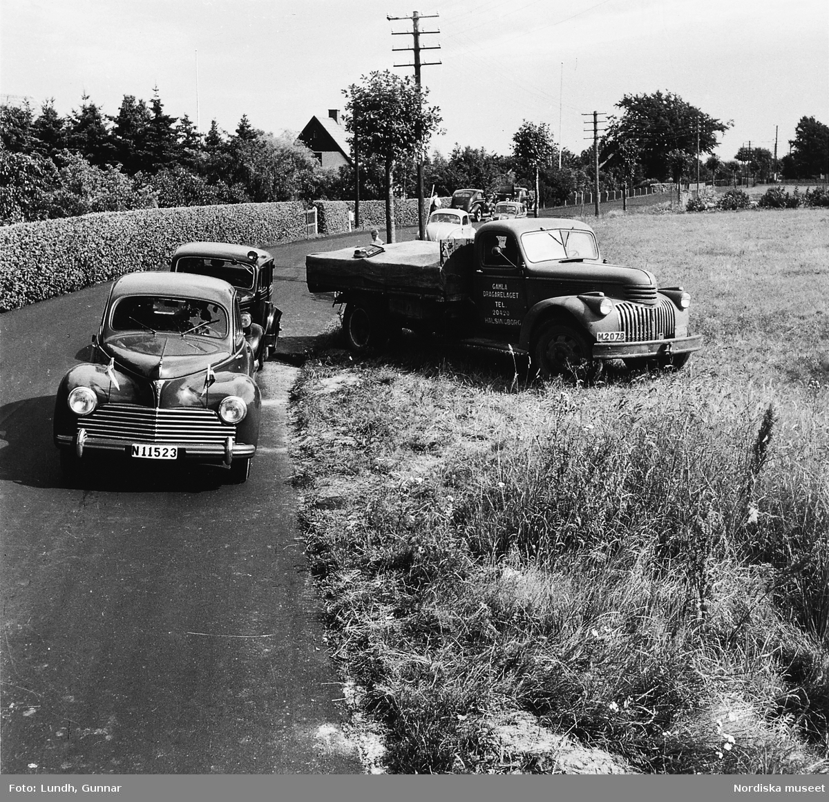 Trafikolycka i Skåne år 1950. Bilar är parkerade längs vägkanten och en lastbil från "Gamla dragarelaget Hälsingborg" står på åkern.