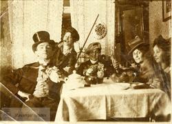 Mann i flosshatt og fire damer rundt et bord